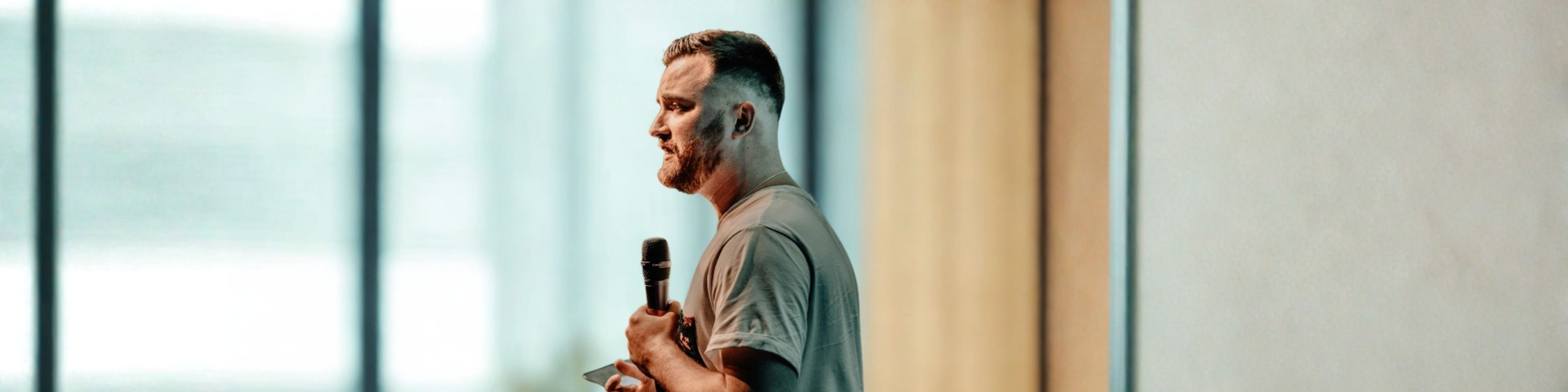 A man holds a microphone and gives a presentation in front of a blurred background
